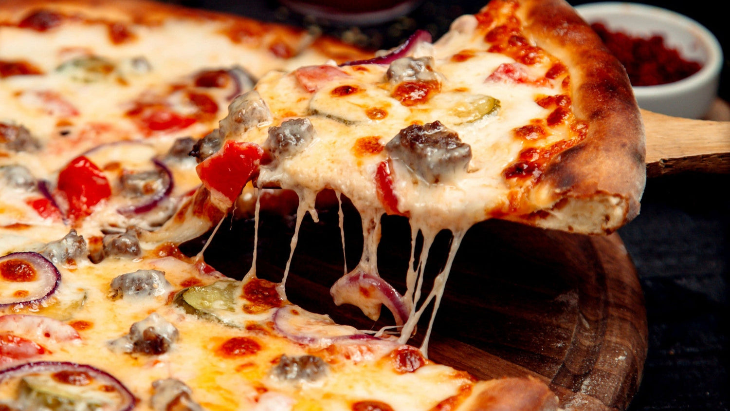 Close-up of a pizza with a slice being lifted, showing melted cheese.