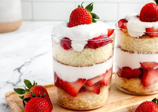 Two layered dessert glasses with strawberries and cream on a marble surface.