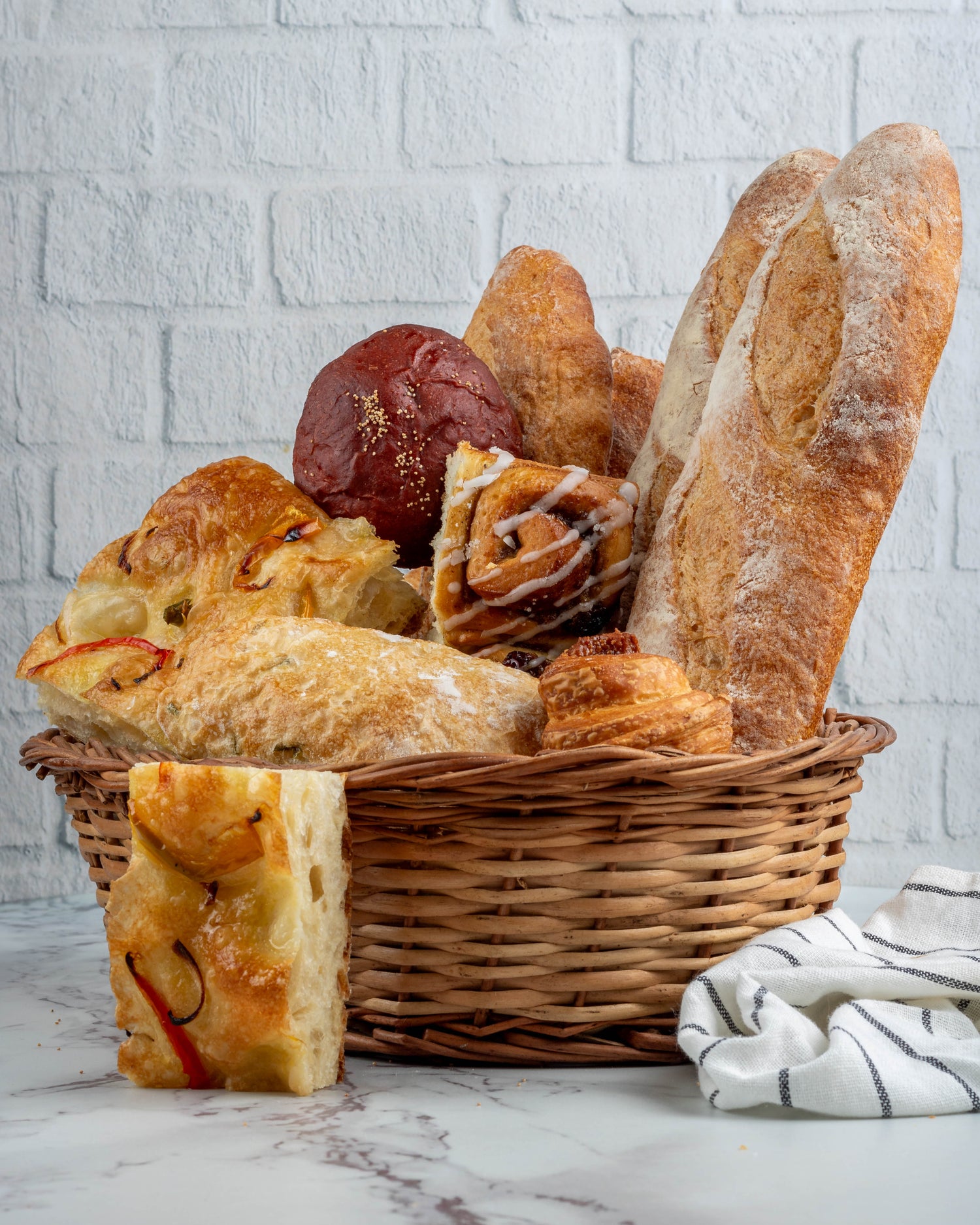 Basket of assorted bread loaves on a marble surface with a white brick wall background