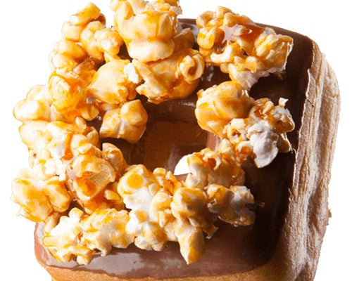 A square frosted donut topped with caramel and popcorn, isolated on a white background.