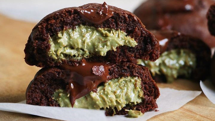 Stack of chocolate cookies with green filling and chocolate drizzle on a wooden surface.