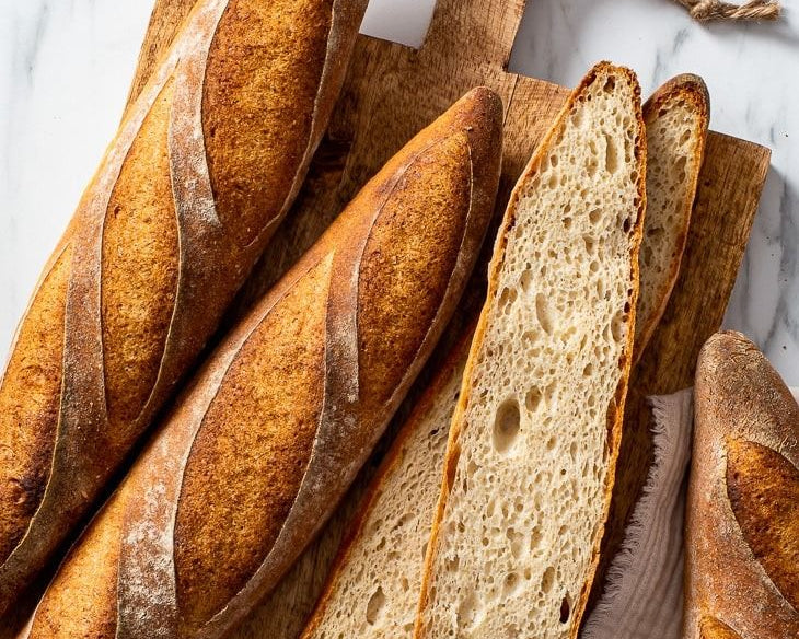 Loaves of bread with a focus on one sliced open, on a white marble surface.