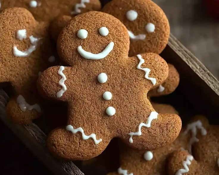 Gingerbread cookies decorated with white icing, arranged in a wooden tray with a festive holiday background.