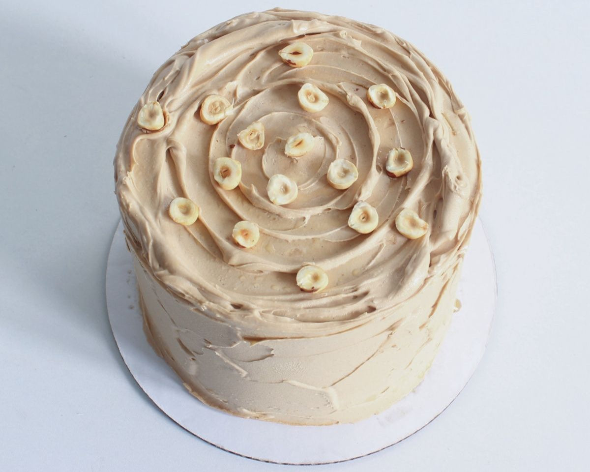 Round cake with beige frosting and decorative elements on a white background