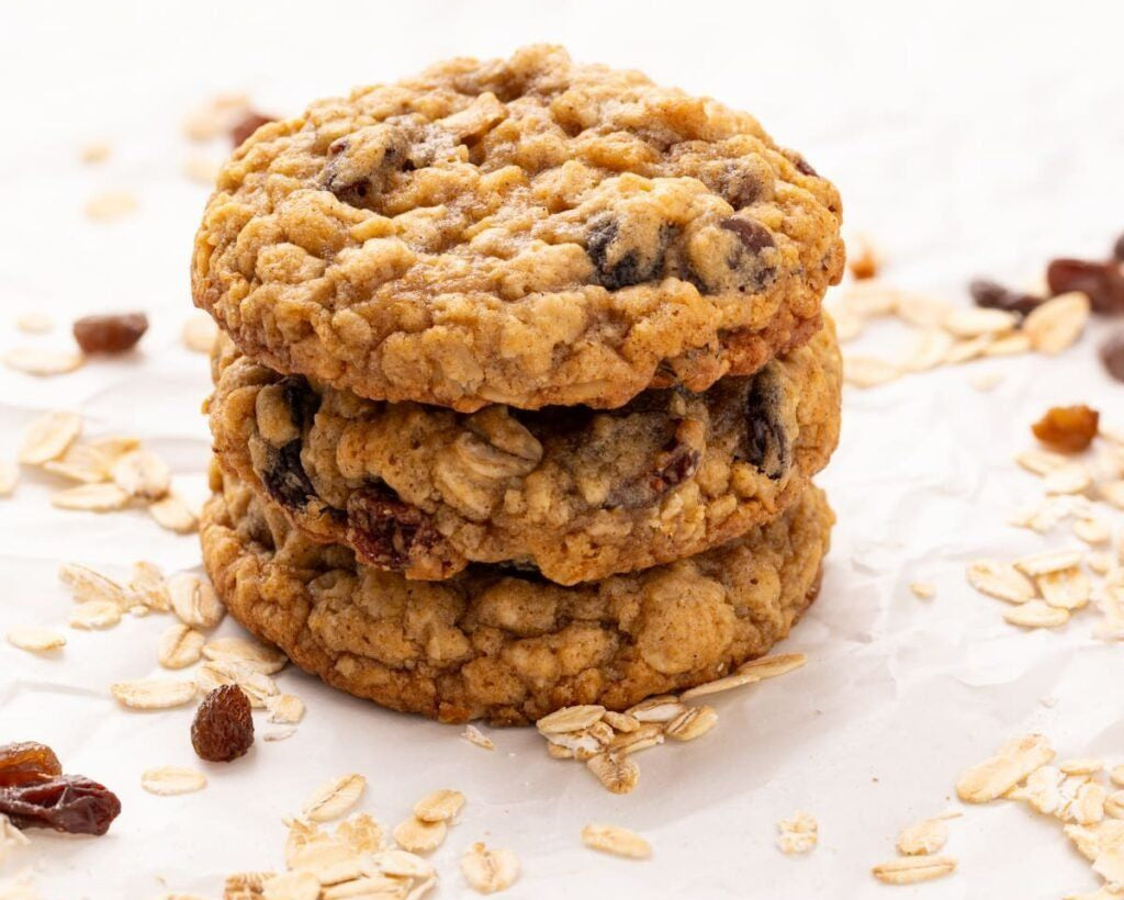 Stack of oatmeal raisin cookies on a white surface with oats and raisins scattered around