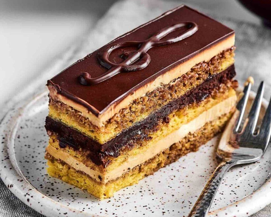 Layered dessert with chocolate ganache on a speckled plate with a fork.