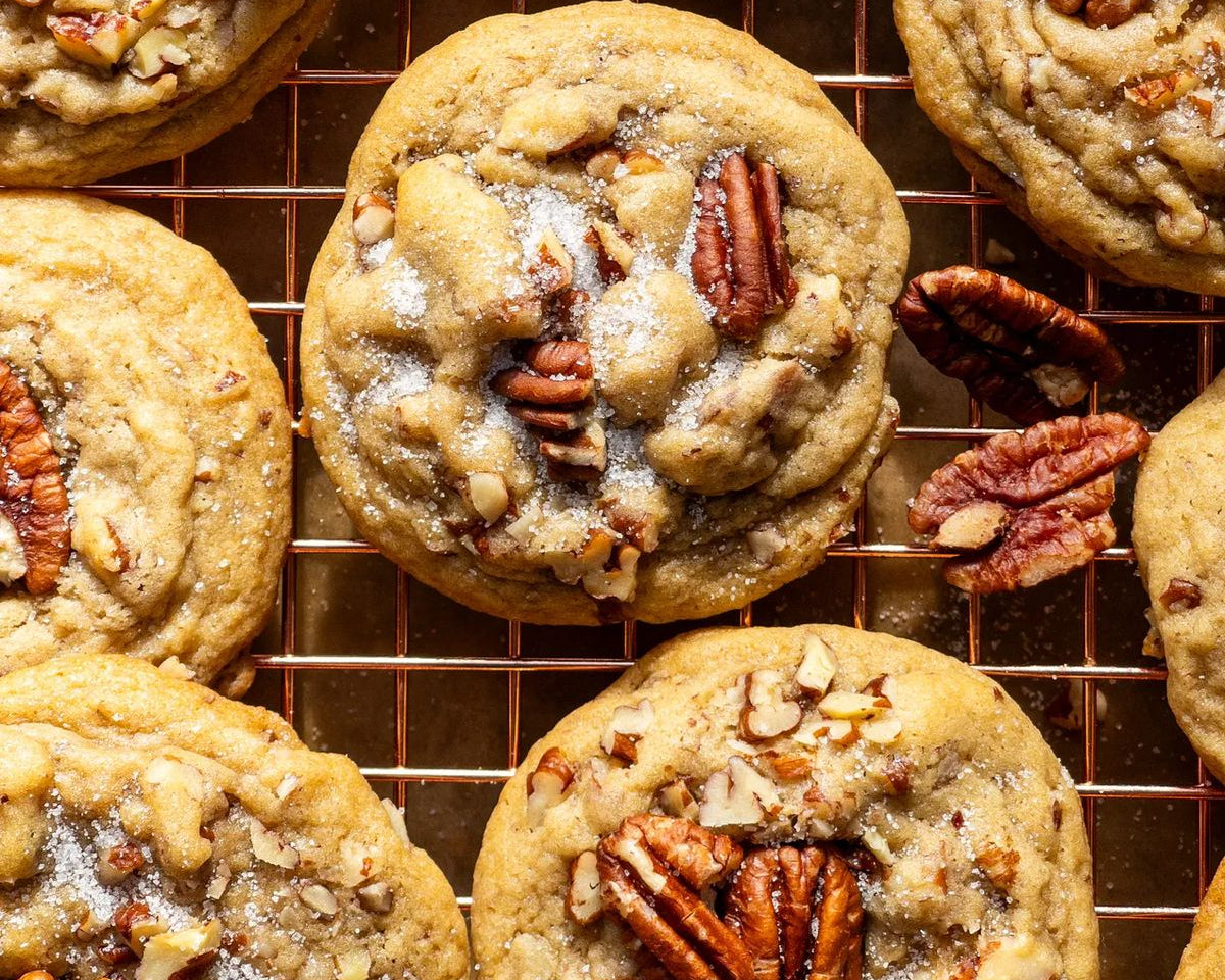 Close-up overhead of several pecan cookies on a metal cooling rack, with chopped pecans and a glaze on the tops.