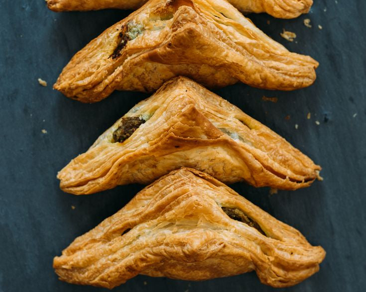 Four golden-brown flaky pastry turnovers arranged vertically on a dark slate background.